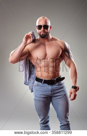 Sexy Muscular Bodybuider With Sunglasses On The Gray Background Throw Off His Shirt