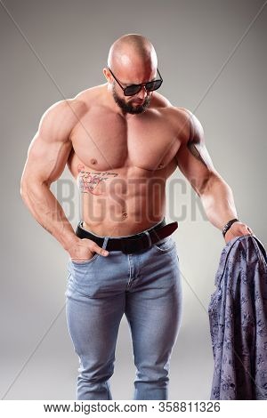 Sexy Muscular Bodybuider With Sunglasses On The Gray Background Throw Off His Shirt