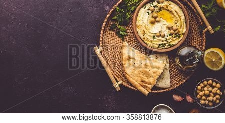 Large bowl of homemade hummus garnished with chickpeas, red sweet pepper, parsley and olive oil