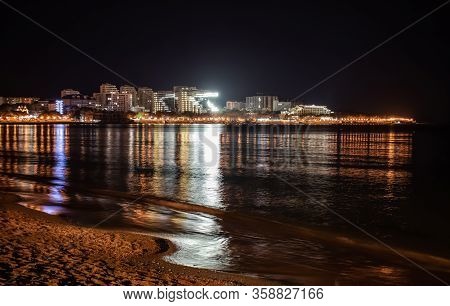 cloudy night view of the bright lights of the building and the city center of the resort of Gelendzhik from the beach. Black sea coast