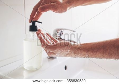 Man Cleaning His Hands Using Liquid Disinfectant Soap And Water In Bathroom.