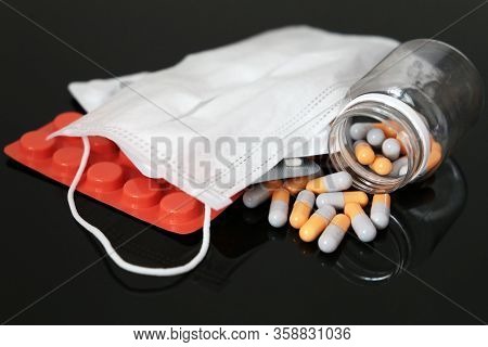 Pills And Capsules In Bottle With Medical Face Mask On Dark Glass Table. Protection And Profilactic 