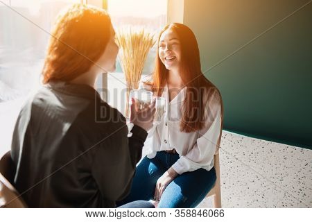 Red-haired Two Young Women Are Talking And Drinking Coffe. Female Models Loughing In A Cafe