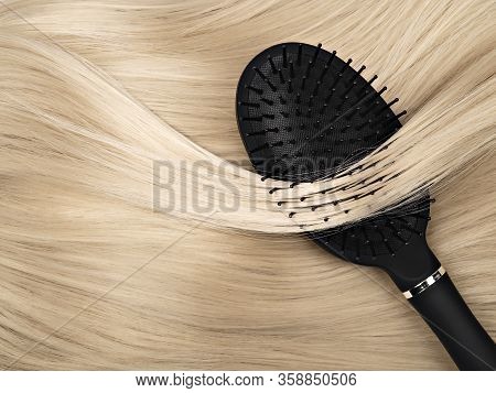 Closeup Of Black Hair Brush Lying On Straight Shiny Blond Hair. Hair Care Concept. Abstract Backgrou