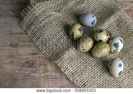 The Quail Eggs Stand On The Burlap On The Wooden Table Next To A Flowerin. Top Views With Clear Spac