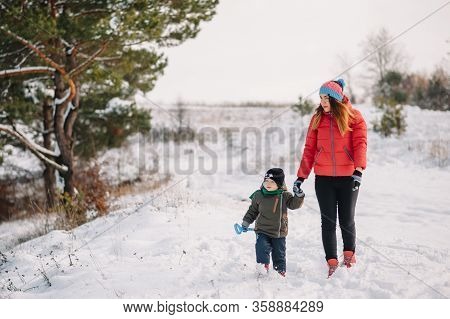 Mother And Little Toddler Boy Walking In The Winter Forest And Having Fun With Snow. Family Enjoying