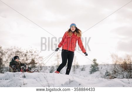 A Father Is Carrying A Child On A Sled. Father Walks With Her Son Over The Snow-covered Forest. Chee