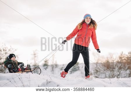 A Father Is Carrying A Child On A Sled. Father Walks With Her Son Over The Snow-covered Forest. Chee