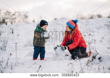 Mother And Little Toddler Boy Walking In The Winter Forest And Having Fun With Snow. Family Enjoying
