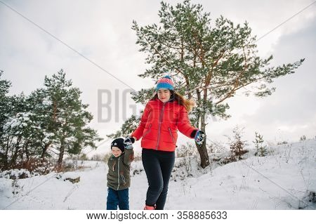 Mother And Little Toddler Boy Walking In The Winter Forest And Having Fun With Snow. Family Enjoying