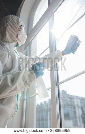 Coronavirus Pandemic. A Disinfector In A Protective Suit And Mask Sprays Disinfectants In House Or O
