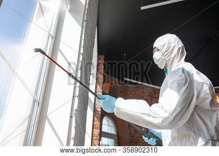 Coronavirus Pandemic. A Disinfector In A Protective Suit And Mask Sprays Disinfectants In House Or O