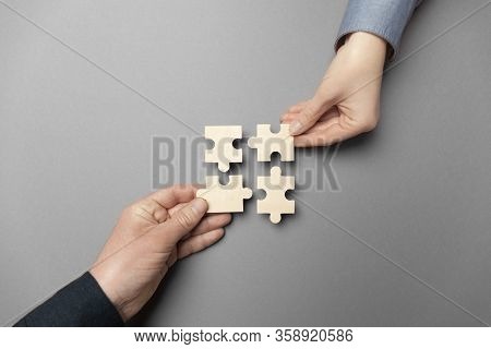 Two Hands Connect Puzzles On A Grey Background. Cooperation And Teamwork In Business. Collaboration 