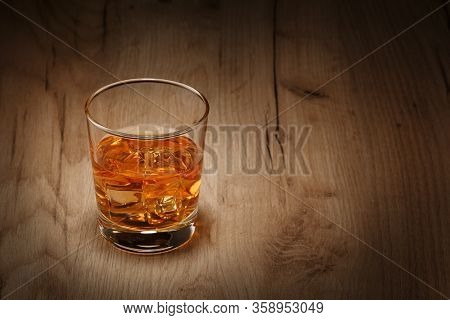 A Glass Of Whiskey With Ice Cubes On A Wooden Table. Space For Text.