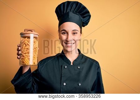 Young beautiful chef woman wearing cooker uniform holding jar with italian pasta macaroni with a happy face standing and smiling with a confident smile showing teeth