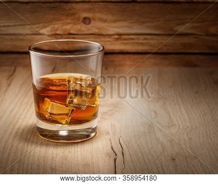 A Glass Of Whiskey With Ice Cubes Is On The Table. Space For Text