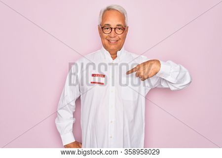 Middle age senior grey-haired man wearing hello my name is introduction sticker with surprise face pointing finger to himself