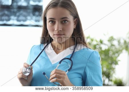 Close-up Of Young Doctor In Uniform Holding Stethoscope. Cute Therapist Looking At Camera With Calmn