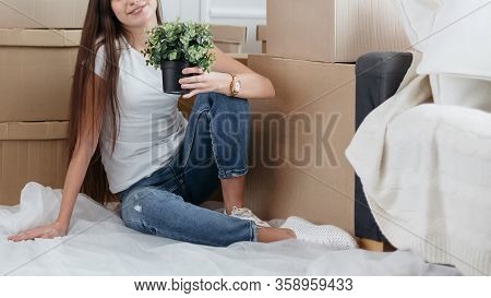 Young Woman With A Home Plant Sitting On The Floor In The New L