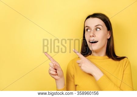 Positive Young Lovely Woman, Points Away With Both Fore Fingers, Demonstrates Copy Space For Your In