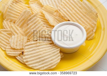 Potato Chips And Dip Served On A Yellow Plate Closeup.  This Snack Food Of Chips And Ranch Dip Is Re