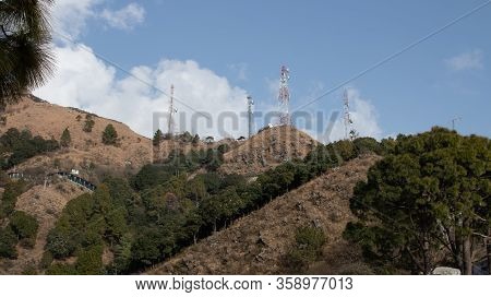 Low Angle Wide Shot Of Telephone Towers Set Up On A Mountain With Trees And Blue Sky In The Backgrou