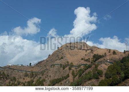 Low Angle Zoomed In Wide Shot Of A Mountain With Shed Covered Roads And Cloudy Blue Sky In The Backg
