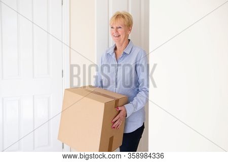 Senior Woman Downsizing In Retirement Carrying Boxes Into New Home On Moving Day