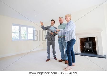 Realtor With Digital Tablet Showing Senior Couple Looking To Downsize Around Retirement Home