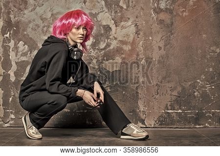 Woman Wear Pink Wig Hair With Headphones, Vintage Filter. Girl In Sport Suit Sit On Hunkers On Abstr
