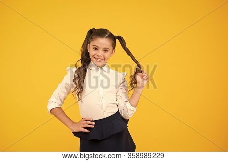 Her Twisted Hairdo. Small Girl Winding Long Hairdoaround Her Finger On Yellow Background. Little Kid