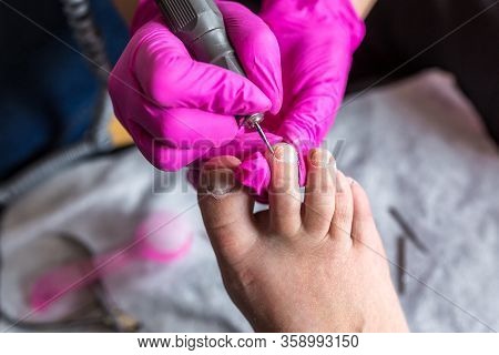 Pedicurist Master In Pink Gloves Cuts The Cuticle And Shellac Toe Nails In The Pedicure Salon Using