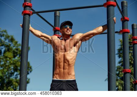 Athletic Sportsman Trains On The Horizontal Bars. Training At The Open Air Sprorts Ground.
