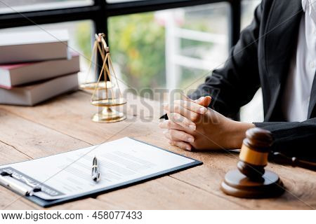 A Woman Lawyer Sits In The Office Of Her Law Firm, On A Table With A Scale Of Justice And A Hammer L