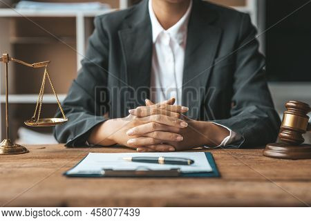 A Woman Lawyer Sits In The Office Of Her Law Firm, On A Table With A Scale Of Justice And A Hammer L