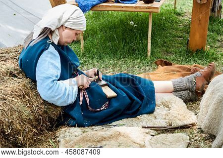 A Woman In Old Roman Clothes Makes Jewelry Sitting On The Grass. Reconstruction Of The Events Of The