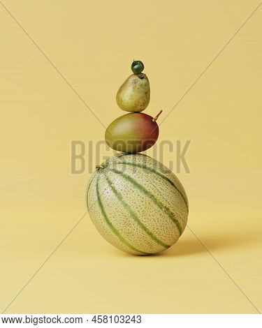 Still Life Pyramid Of Melon, Pear, Mango And Tomato On A Yellow Background. Ripe Fruit And Vegetable