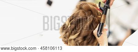 Close-up Of Blonde Female On Hairdresser Appointment Get Curly Hairstyle. Master Use Curling Iron To