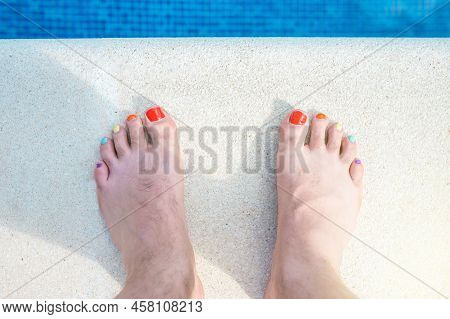 Feet Of A Hairy Man With His Nails Painted In Lgbtiq Colours. Bare Feet At The Edge Of A Swimming Po