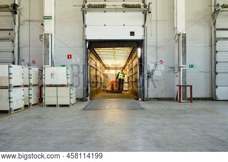 Interior Of A Modern Warehouse Storage Of Retail Shop With Pallet Truck Near Shelves And Loading Ram