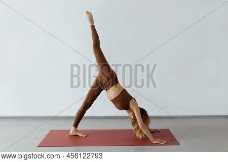 Slender Young Woman Practicing Downward Facing Dog Asana With Leg Raised, Ekapada Adhomukha Shvanasa
