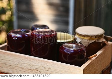 Close-up Of Wooden Crate With Homemade Berry Confiture In Jars Standing Upside Down Against A Wooden