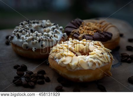 Three Doughnuts Covered With Almendras, Cookies And Creme And Choco Peanut Butter On Wooden Cutting 