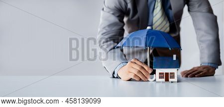 Individuals Holding Small Umbrellas And Model Homes, Housing Insurance Against Impending Loss And Fi