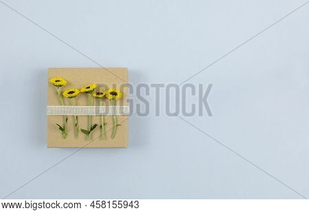 Top View On Square Brown Gift Box With Yellow Flowers Attached To It With The Ribbon. Lay Flat On Li