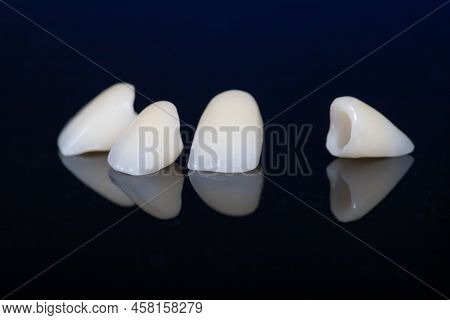 Four Dental Crowns Zirconia On A Mirror Table, Black Background. Crowns For Front Teeth