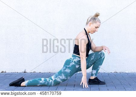 Beautiful Young Blonde Fitness Woman Wearing Black And Blue Sports Clothes Stretching And Warming Up