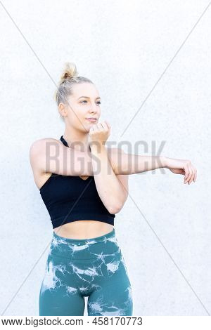 Sporty Young Blonde Fitness Woman Wearing Black And Blue Sports Clothes Stretching Arms And Shoulder