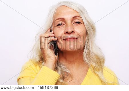 Elderly Woman Wearing Yellow Sweater With Smartphone Over White Grey Background.