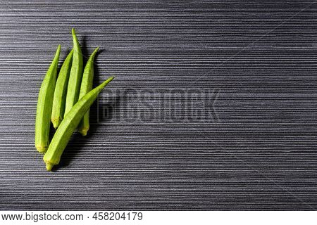 Fresh Ochra, Bhindi Or Ladies Fingers Whole And Uncooked Against A Grey Horizontal Stripped Backgrou